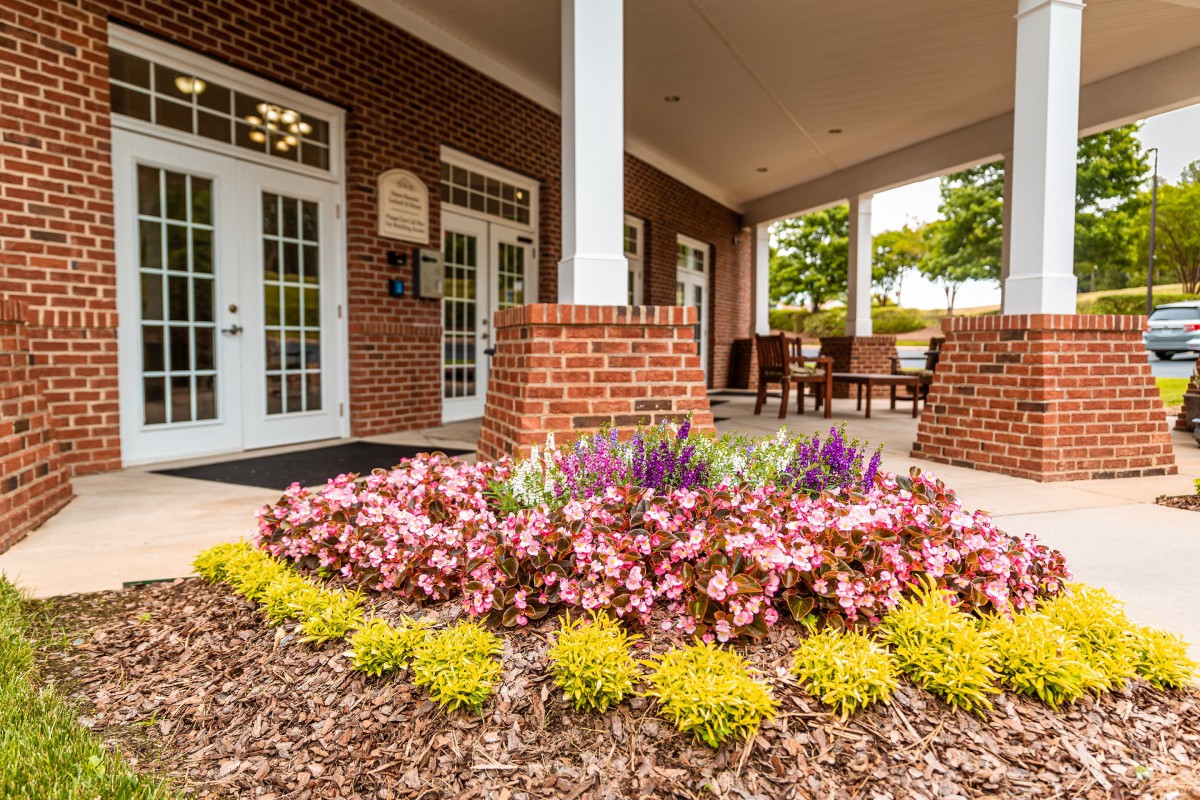 The entrance features a beautifully landscaped garden with blooming flowers in front of a brick building.