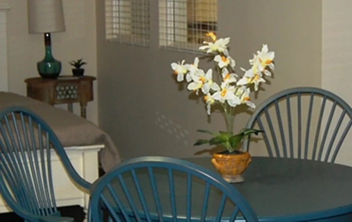 A cozy interior featuring a dining table with blue chairs and a vase of white flowers.