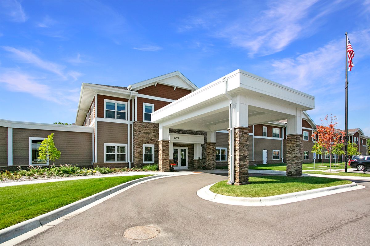 A modern residential building with a covered entrance and driveway under a clear blue sky.