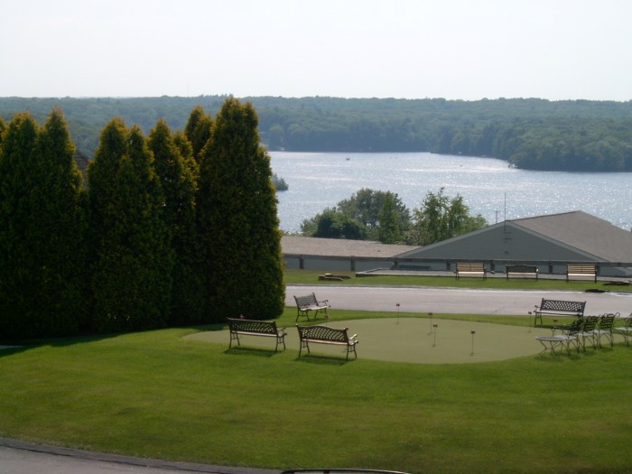 A serene view of a lake surrounded by trees, with benches and buildings in the foreground.
