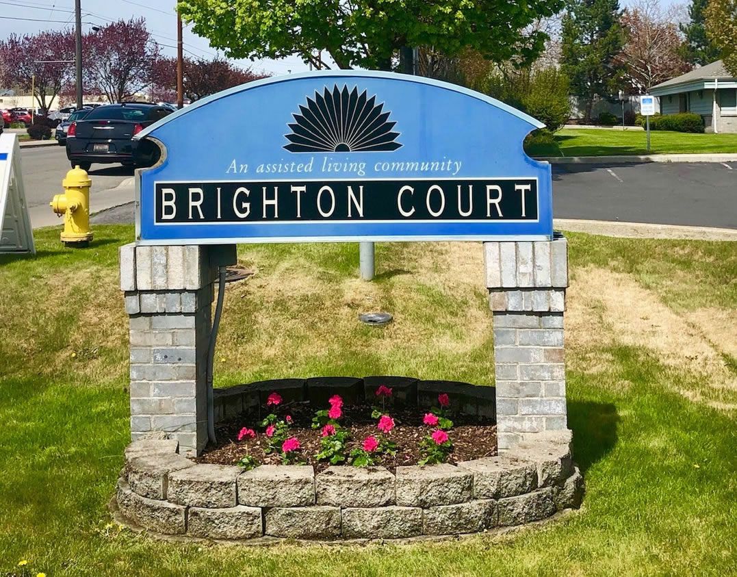 A community sign for Brighton Court, set against a backdrop of greenery and flowers.