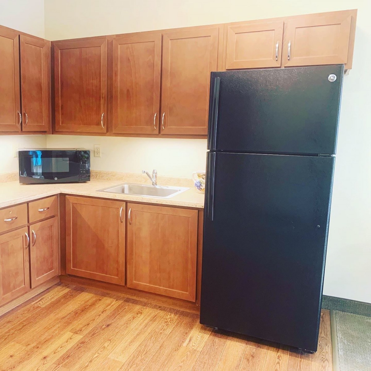 A modern kitchen with wooden cabinets, a black refrigerator, and a microwave on the countertop.
