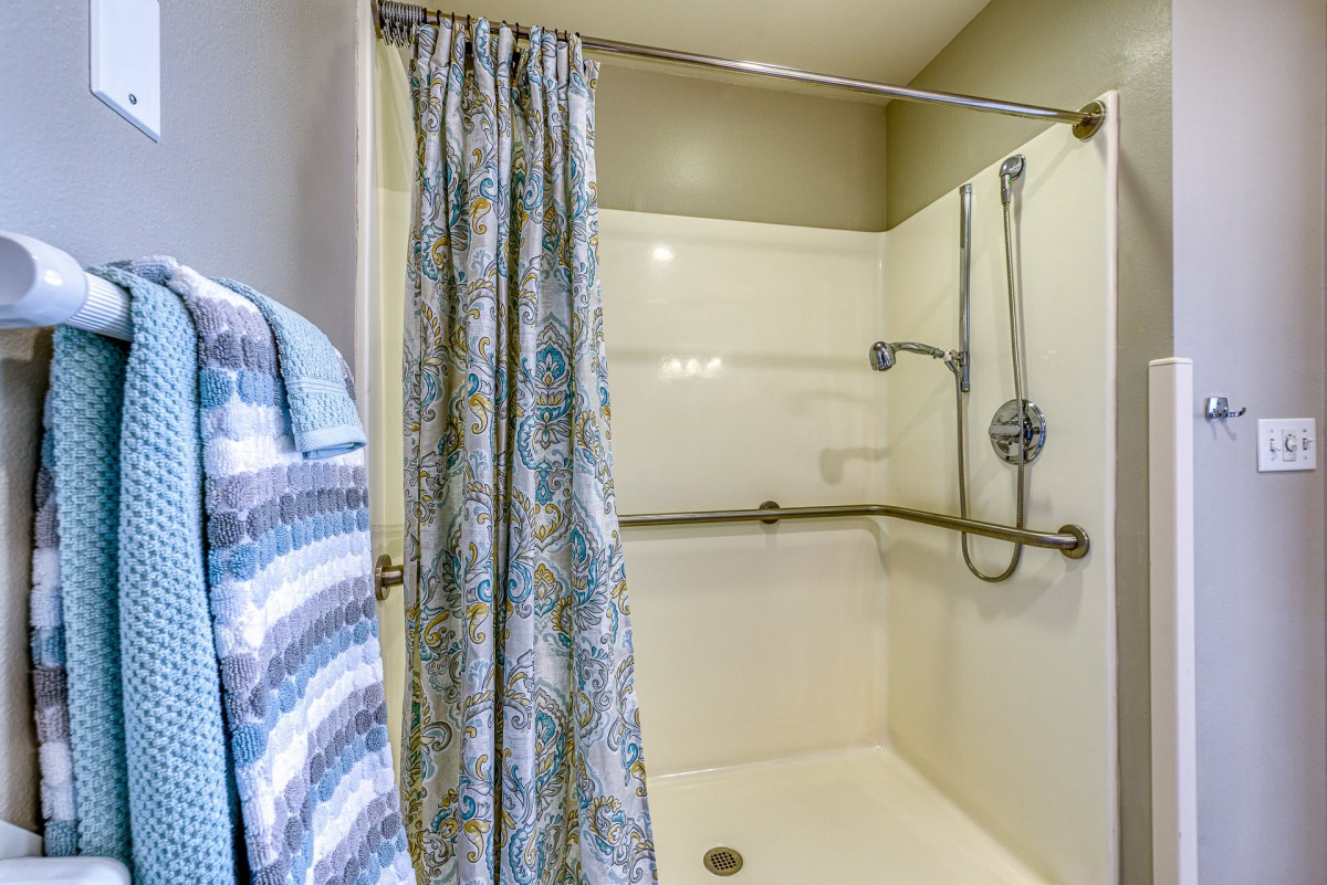 A bathroom featuring a shower area with a curtain and grab bars.