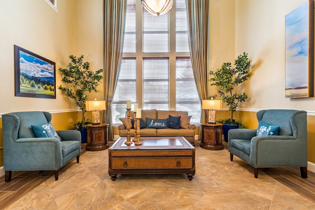 A luxurious living room featuring a central sofa, armchairs, and a wooden coffee table, complemented by tall windows and decorative plants.