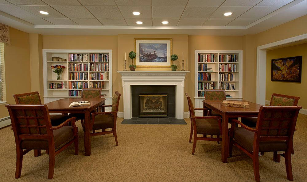 A cozy library with bookshelves, a fireplace, and seating for reading.