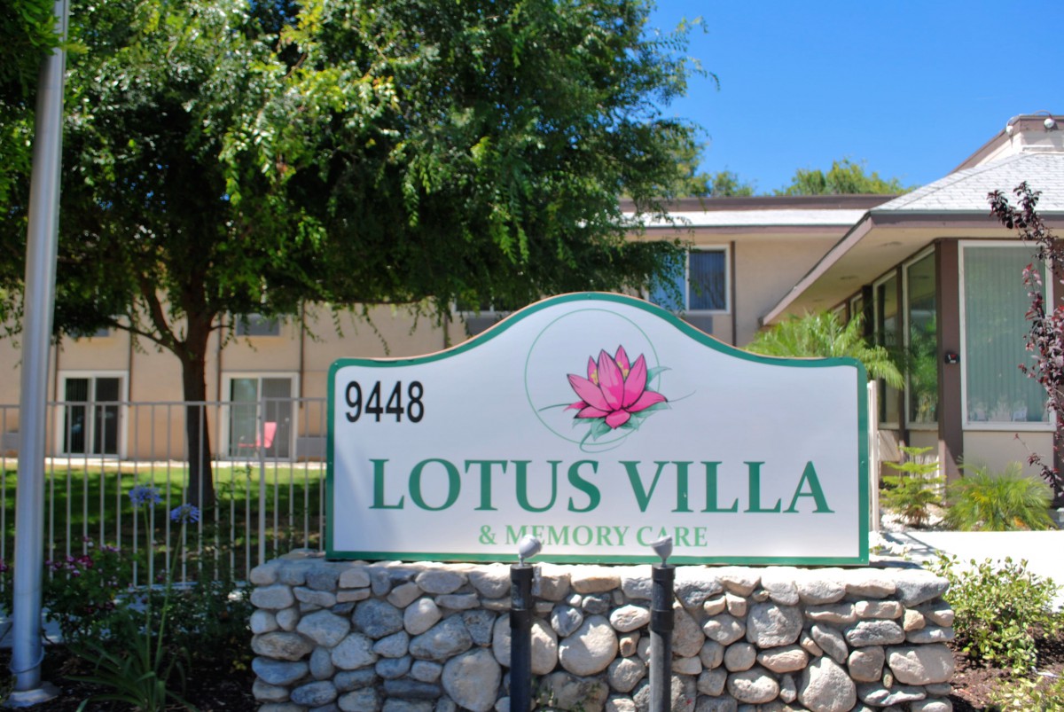 A sign for Lotus Villa in front of a residential building with trees and a stone base.