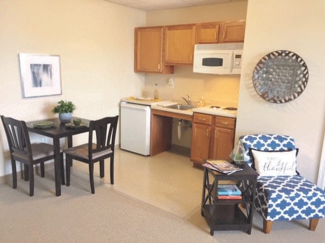 A cozy apartment with a small kitchen and dining area, featuring wooden cabinets, a microwave, refrigerator, and a table with chairs.