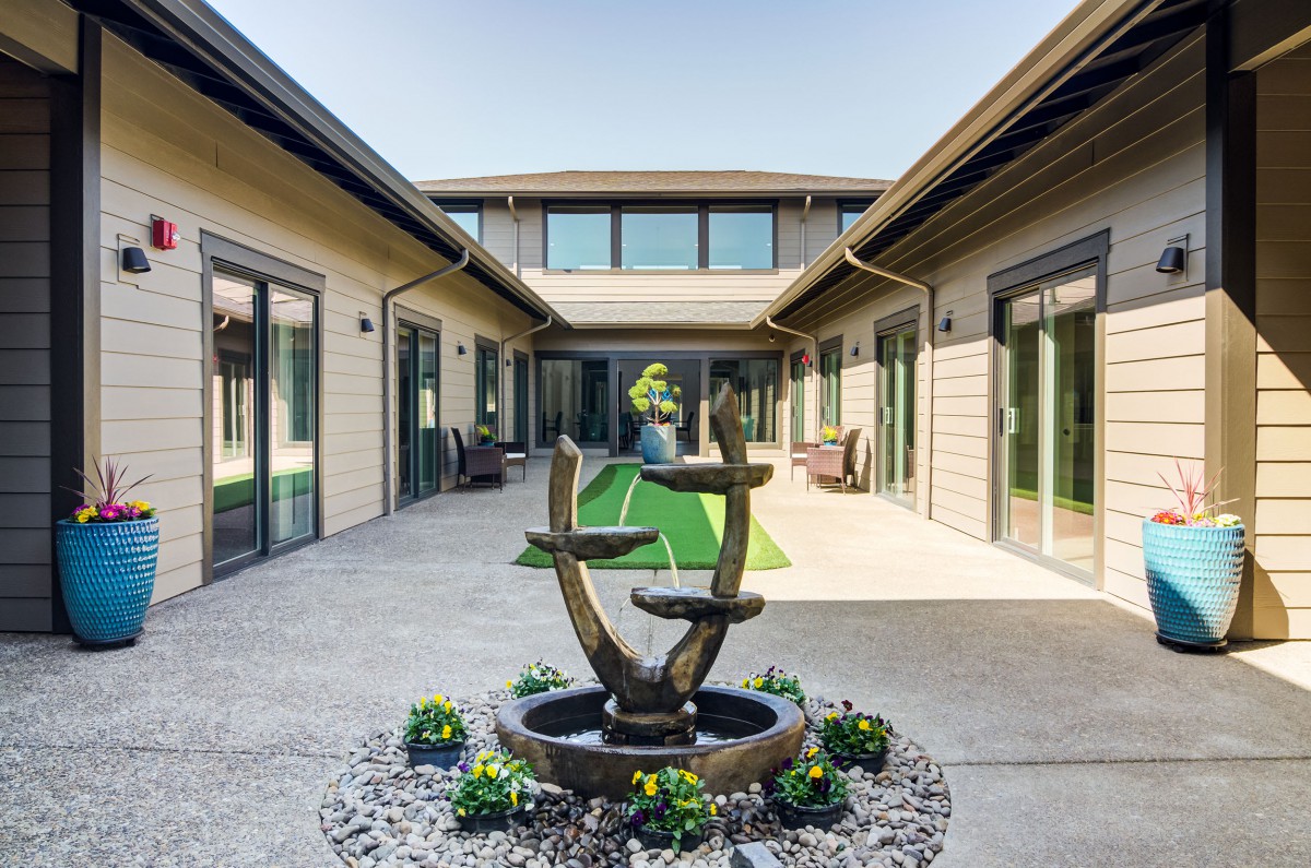 A modern courtyard with a unique fountain centerpiece and surrounding greenery.