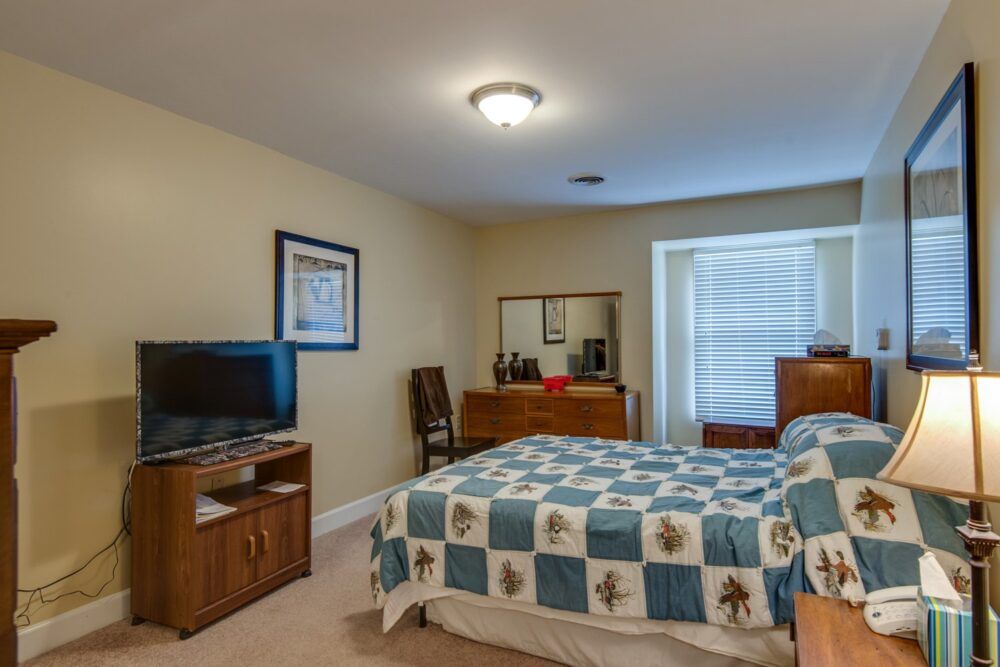 A cozy bedroom with a bed, dresser, and television setup.