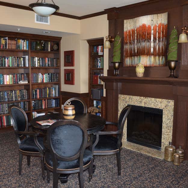A cozy library room featuring a collection of books, a fireplace, and a seating area with a table and chairs.