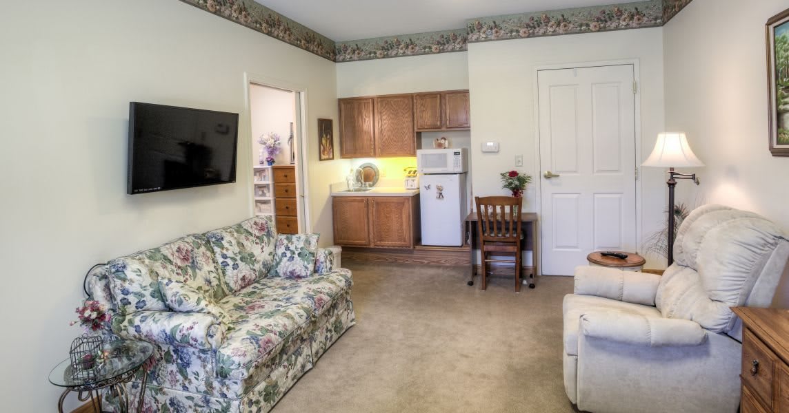 A cozy living room with a floral-patterned couch and a small kitchenette.