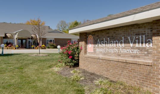 A brick building with a sign in front, surrounded by plants and a landscaped area.