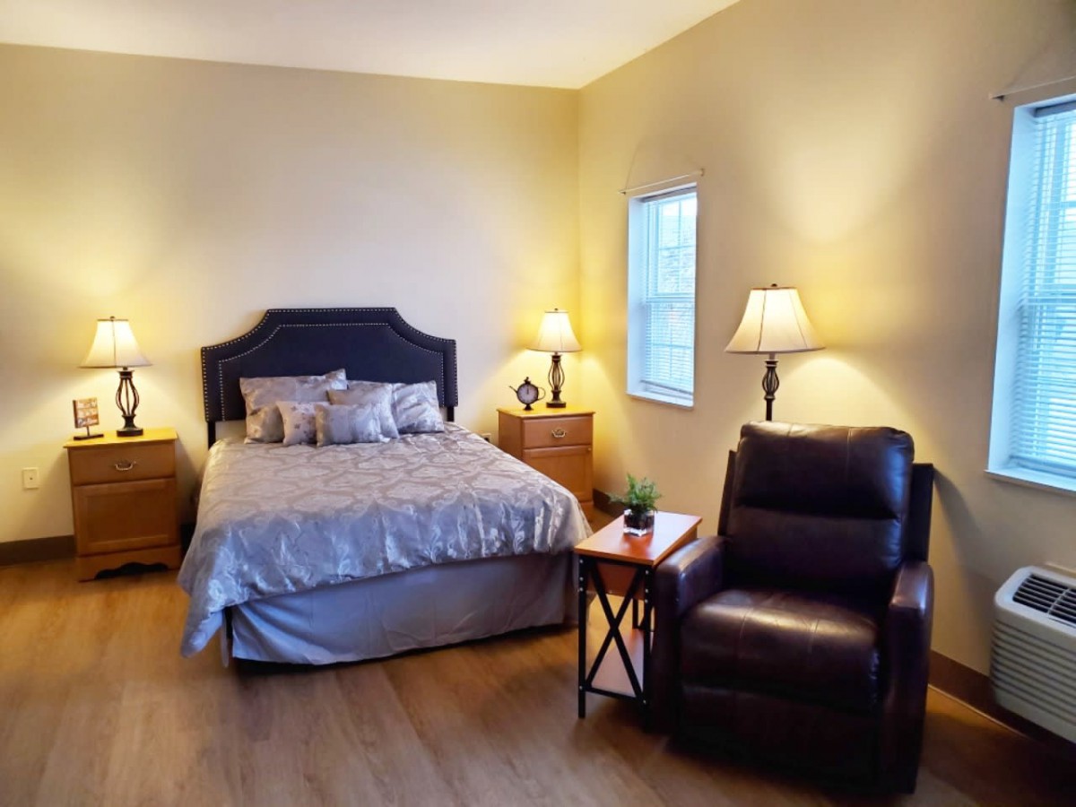 A cozy bedroom with a neatly made bed, accompanied by a comfortable chair and warm lighting from the lamps on the nightstands.