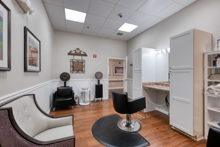 A neatly organized salon room with a chair, mirror, hair dryer, and bright lighting.