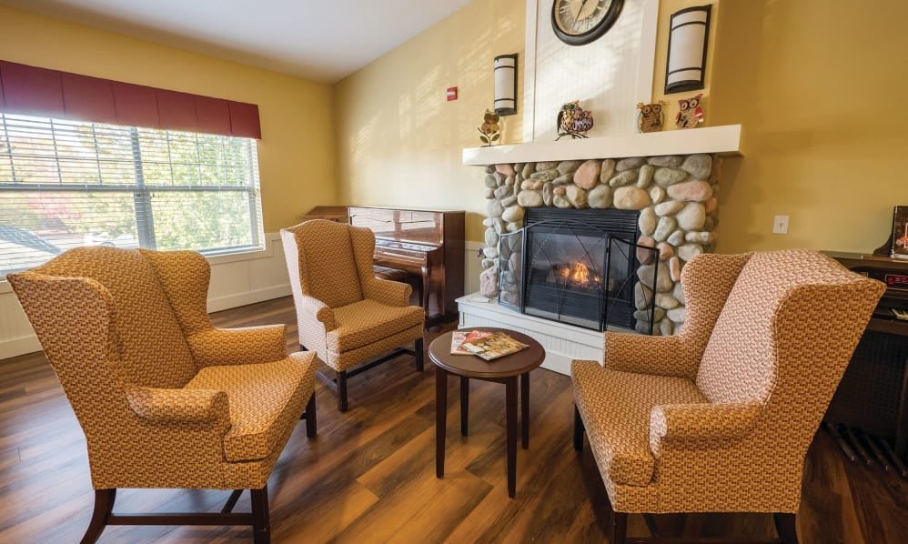 A cozy living room with a stone fireplace, surrounded by armchairs and wooden flooring.