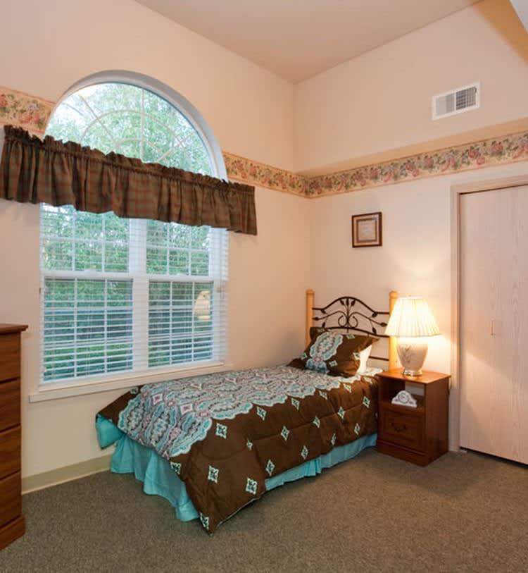 A cozy bedroom with a single bed, nightstand, and window.