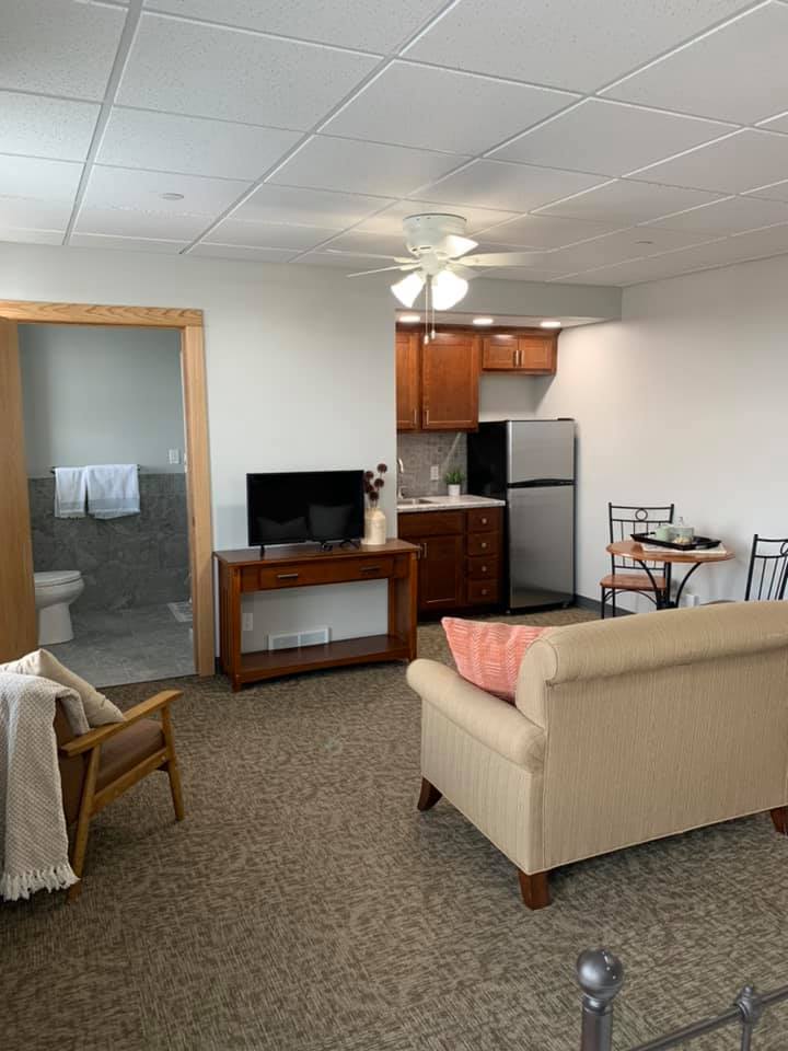 A cozy living space with a kitchenette, sofa, television, dining table, and an adjoining bathroom.