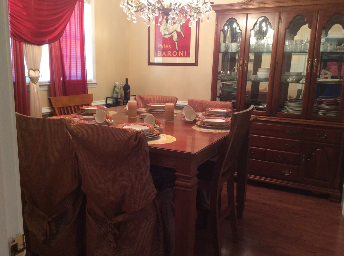 A cozy dining room with a wooden table and chairs set for dinner, illuminated by a chandelier.