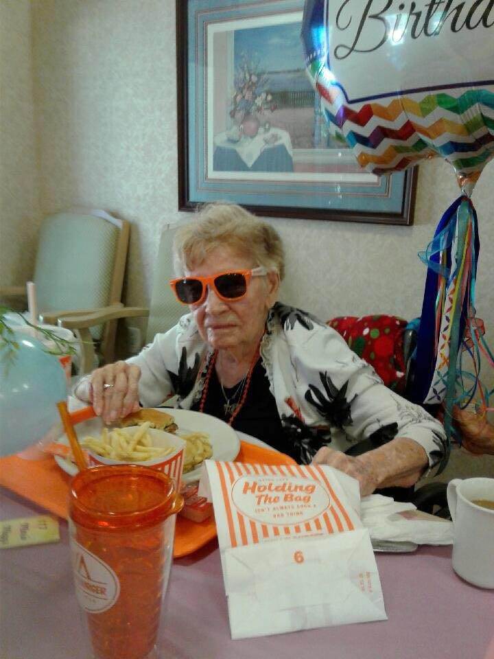 Elderly woman enjoying a meal at Whataburger with festive balloons in the background.