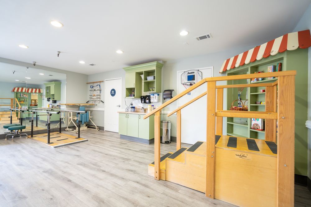 A spacious children's playroom with colorful furniture and educational materials, featuring a wooden staircase and green cabinets.