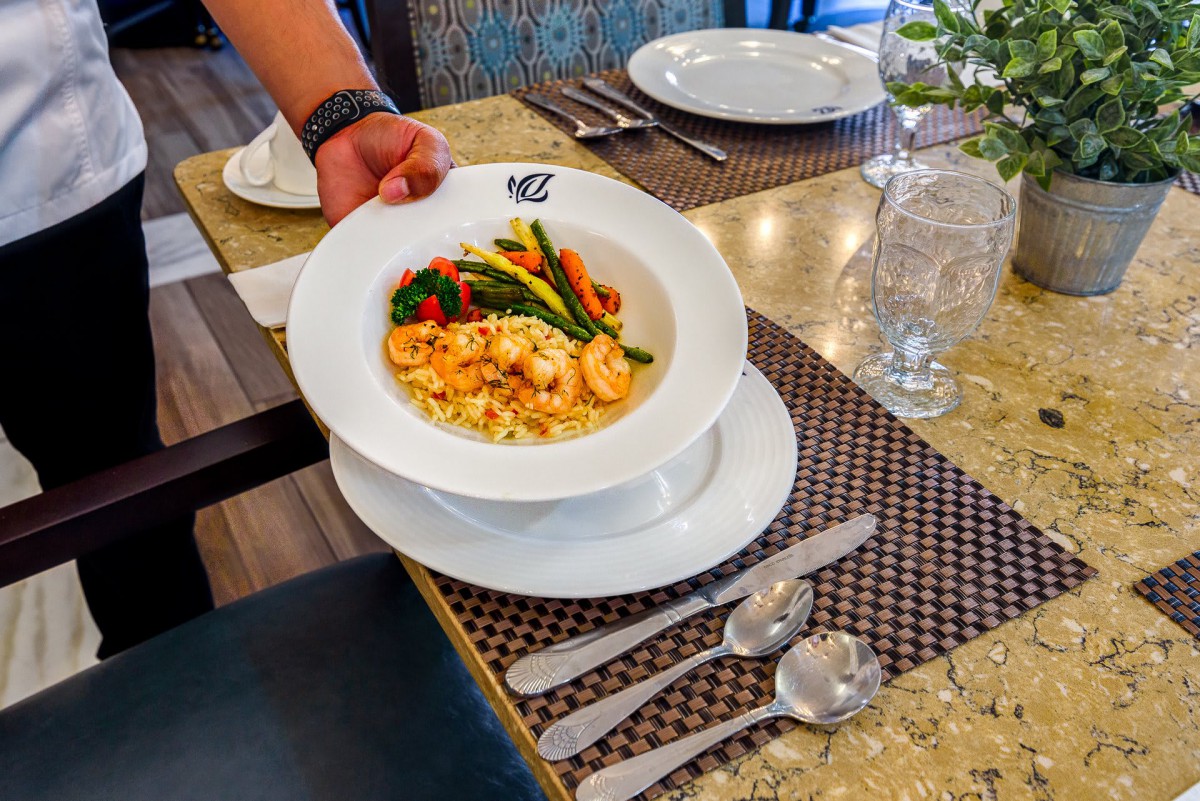 A bowl of pasta with shrimp and vegetables being served at a restaurant.