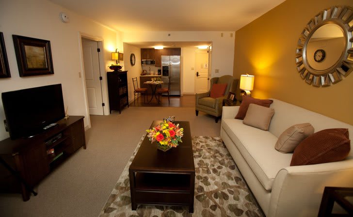 A cozy living room with modern decor, featuring a white sofa and a central coffee table adorned with flowers.
