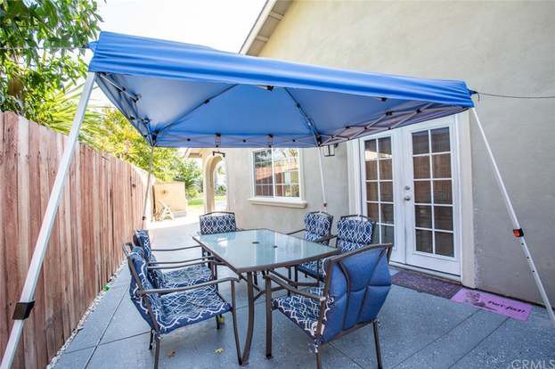 A backyard patio setup with a blue canopy providing shade over a glass table and six cushioned chairs.