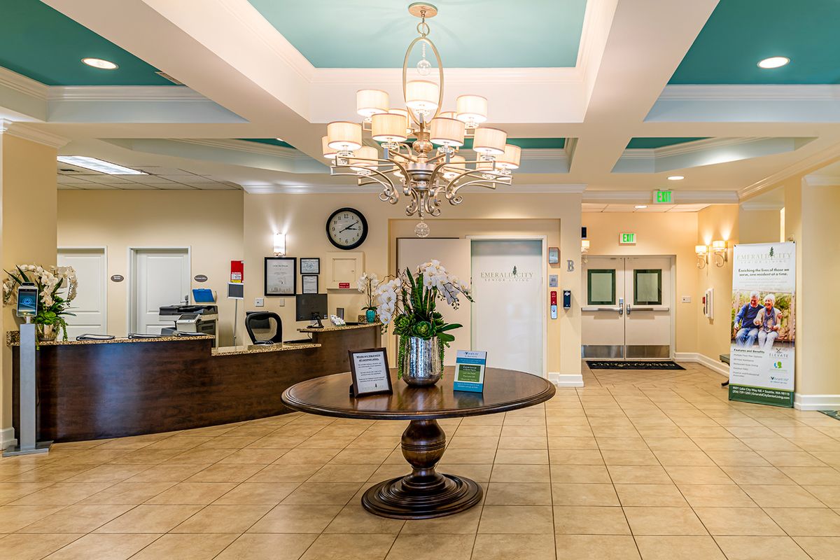 A well-lit lobby with a chandelier, reception desk, and central table adorned with plants.