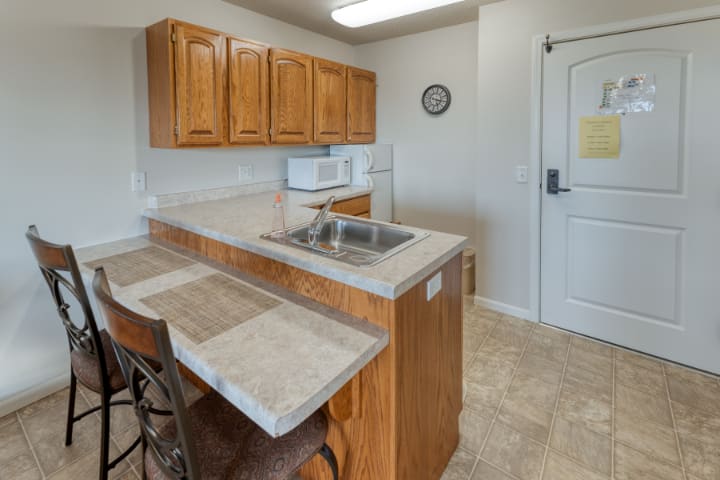A small kitchen area with wooden cabinets and a countertop, featuring a microwave and sink.