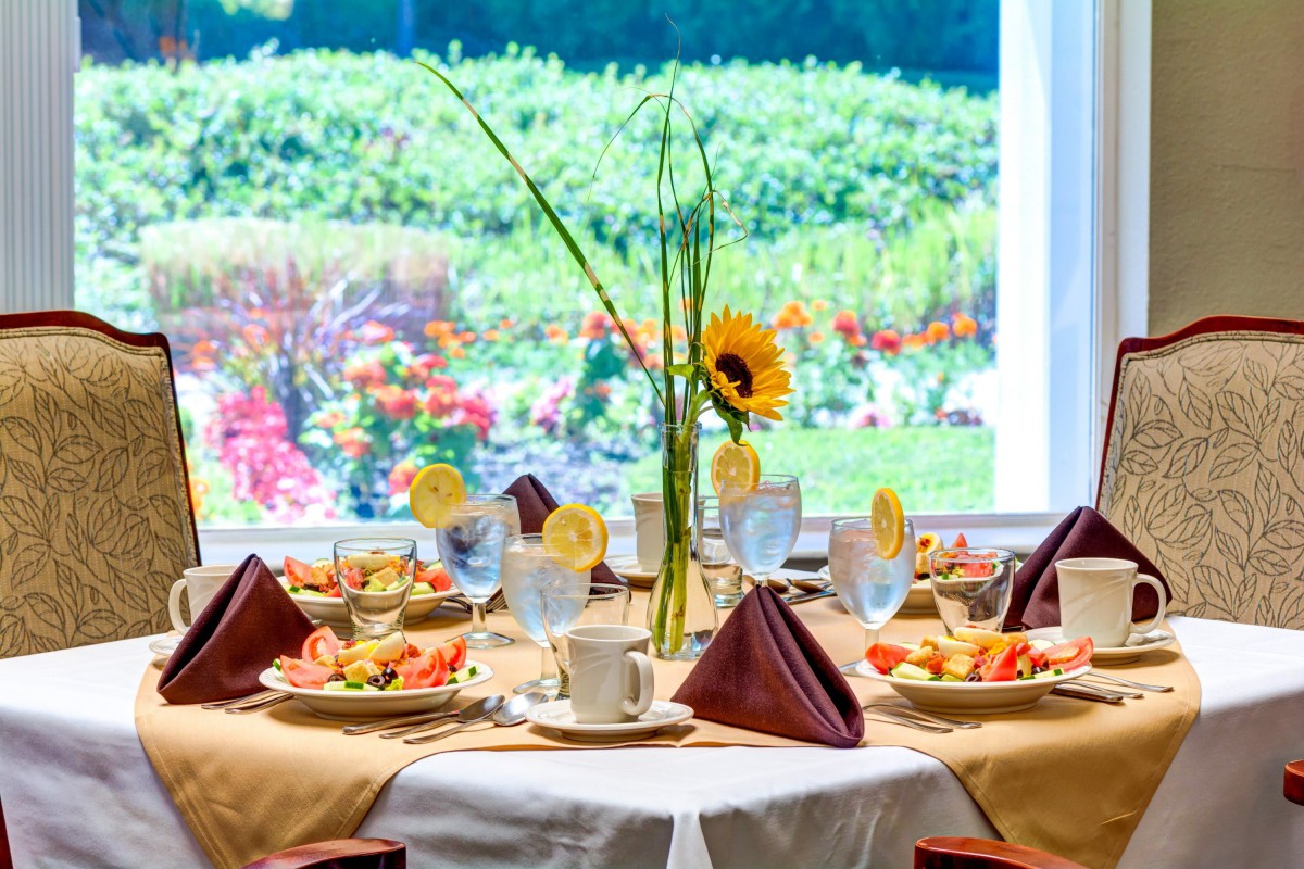 An elegantly set dining table with floral decor overlooking a vibrant garden.
