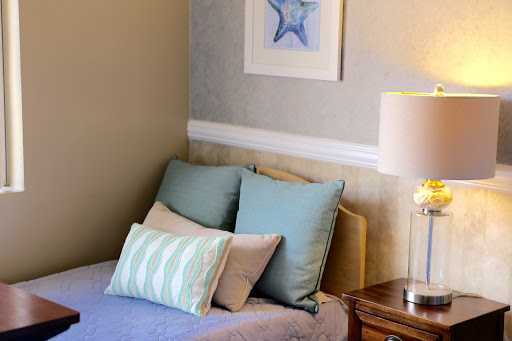 A cozy corner of a bedroom showcasing a neatly made bed with decorative pillows, accompanied by a bedside lamp and wall art.