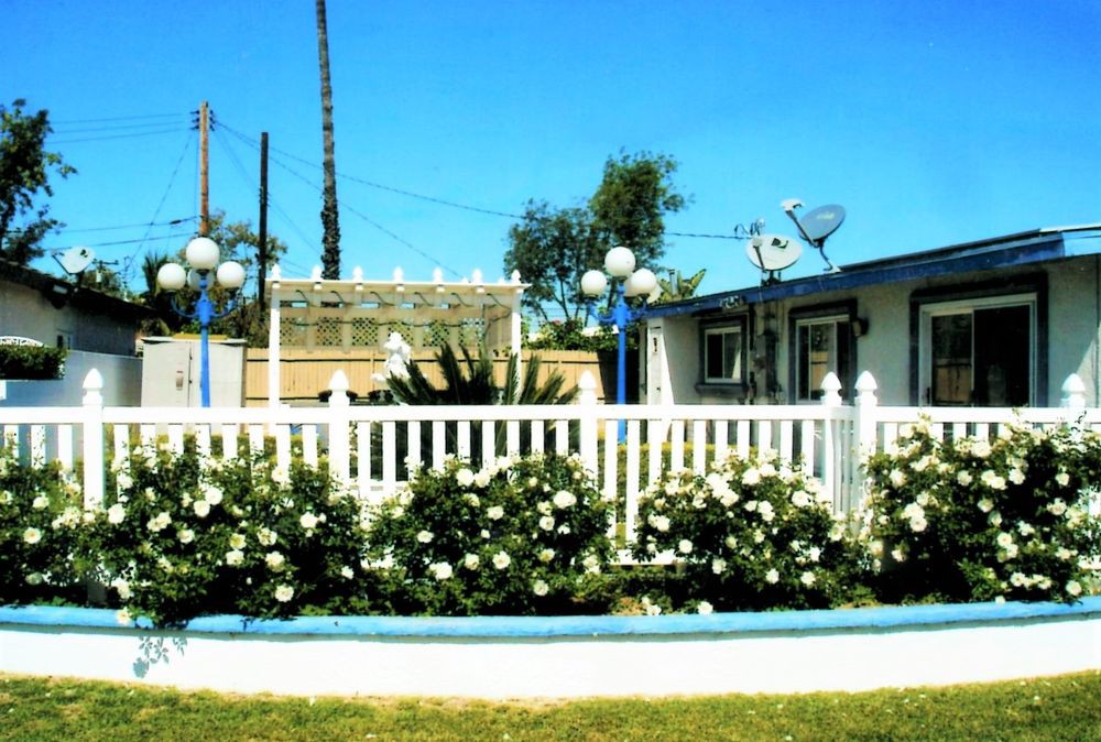 A white fence surrounds a garden with blooming flowers in front of a house.