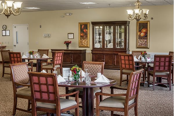 An elegantly decorated dining area with neatly arranged tables and chairs, featuring a chandelier and floral centerpieces.