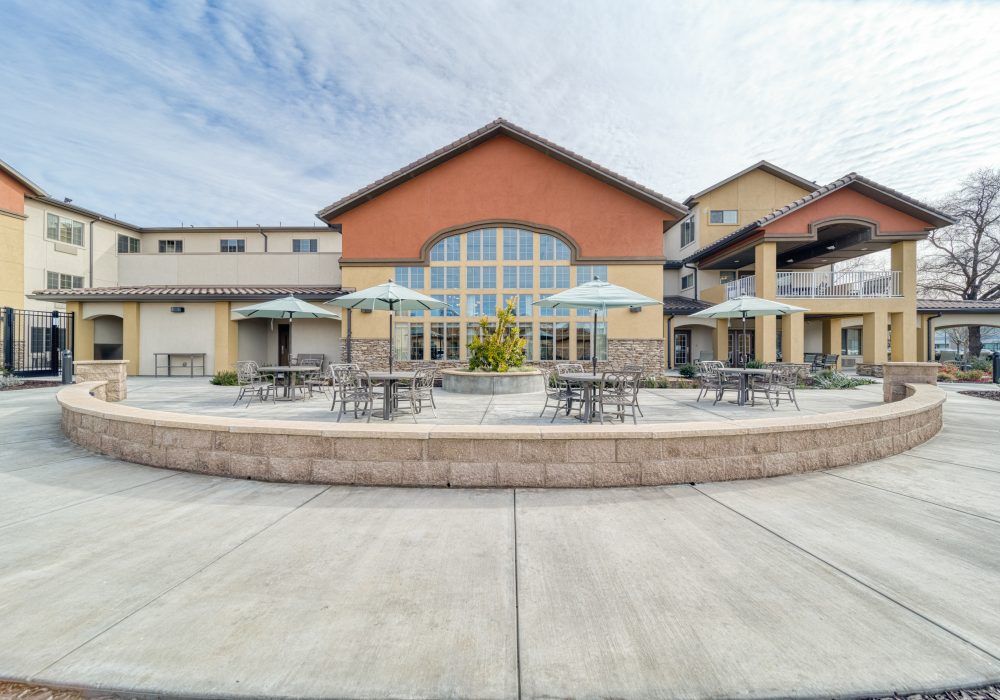 An outdoor patio area with tables and umbrellas in front of a commercial building.