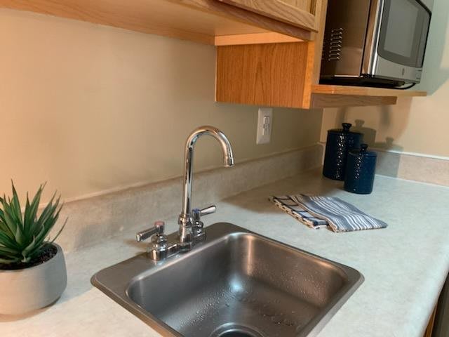 A modern kitchen with a stainless steel sink and faucet, featuring neatly arranged countertop items and wooden cabinets.