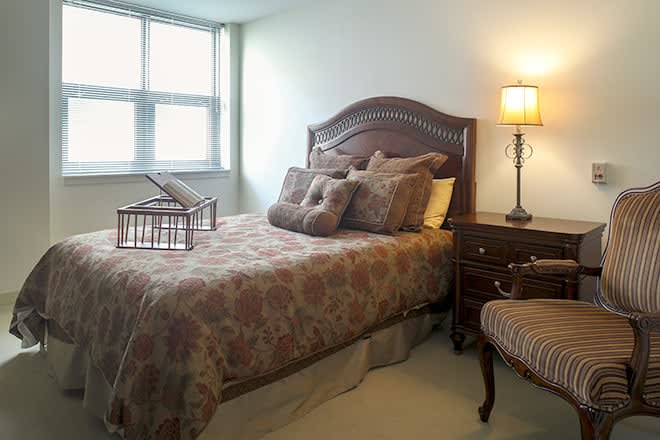 A cozy bedroom with a bed, lamp, and window providing natural light.