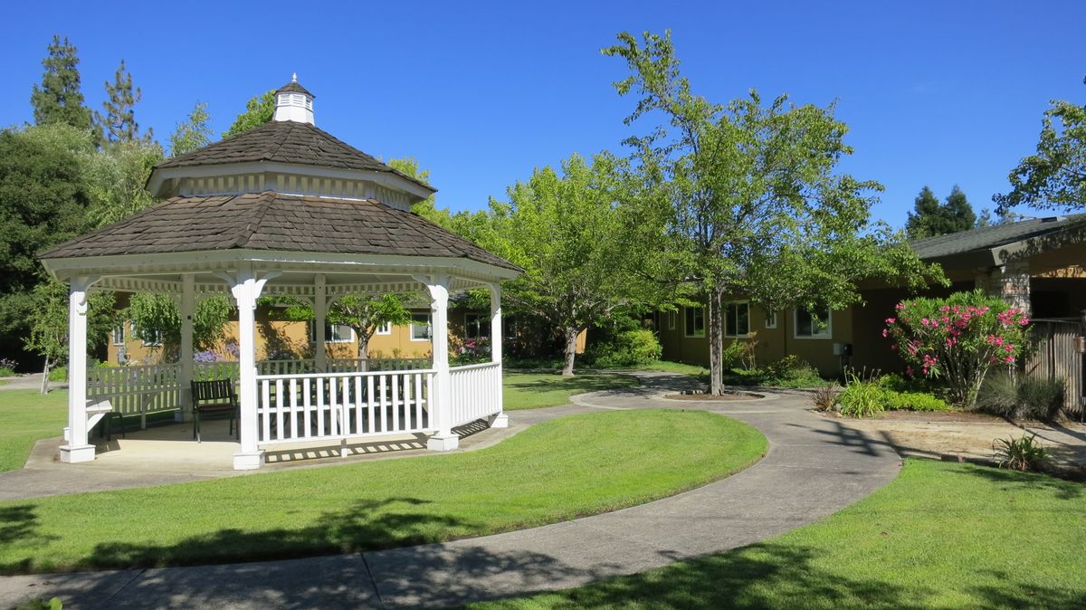 A serene park with a gazebo and winding pathways under a clear blue sky.