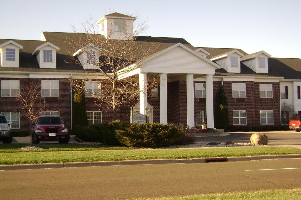 A large brick residential building with white columns and a landscaped front yard.
