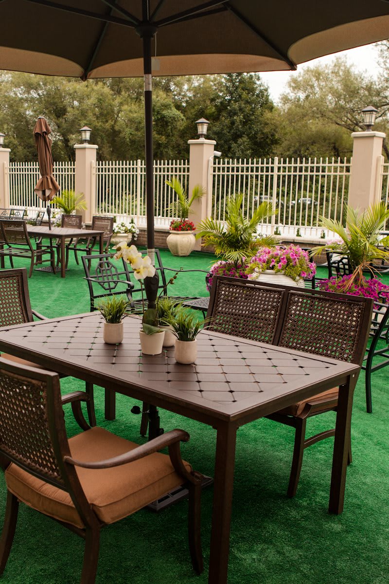 A peaceful outdoor patio with metal tables and chairs, surrounded by lush greenery and potted plants.