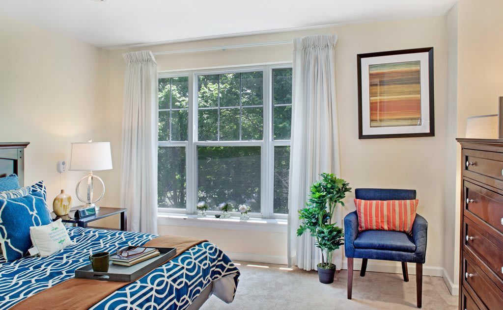 A bright and cozy bedroom with a large window, modern decor, and a comfortable seating area.