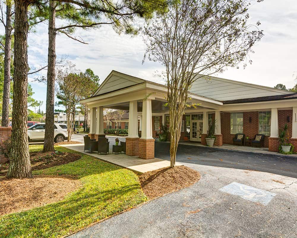 A building entrance with a covered walkway surrounded by trees and landscaping.