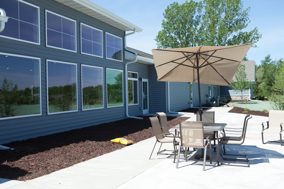 A modern home with large windows and an outdoor patio area featuring a table, chairs, and an umbrella.