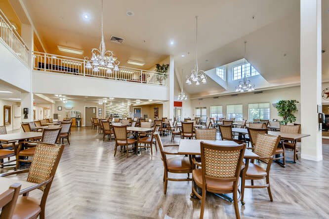 A spacious dining area with elegant chandeliers, wooden tables, and chairs on polished wood flooring.