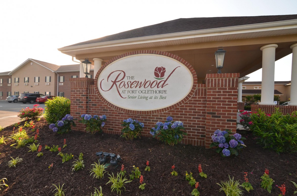 A brick entrance sign for Rosewood Retirement with neatly landscaped flowers and shrubs.