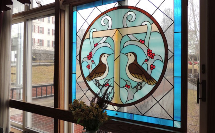 A decorative stained glass window featuring two birds surrounded by floral designs.