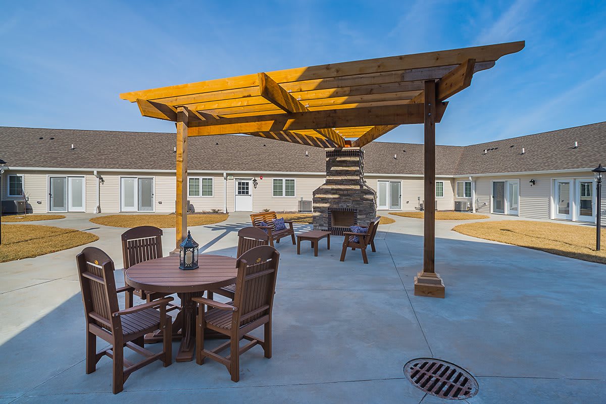 A spacious patio area featuring wooden furniture, a pergola, and an outdoor fireplace.