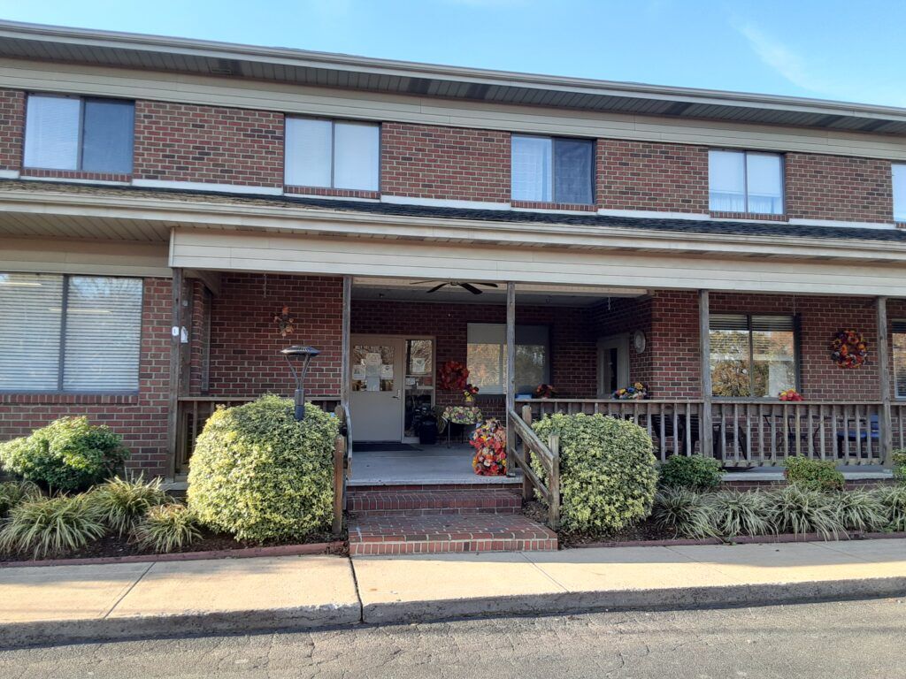 A two-story brick residential house with a porch and well-maintained shrubs.