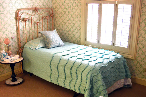 A cozy single bed with a textured quilt and a decorative pillow, set against a patterned wall.