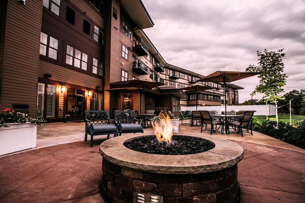A cozy outdoor patio area with a fire pit and comfortable seating in front of an apartment building.