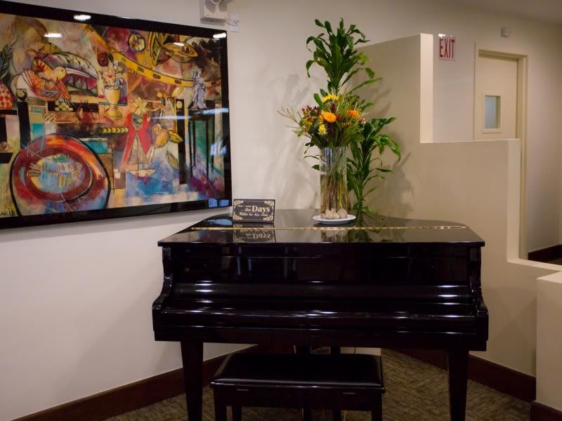 A grand piano adorned with a floral arrangement is set against a backdrop of colorful abstract art.